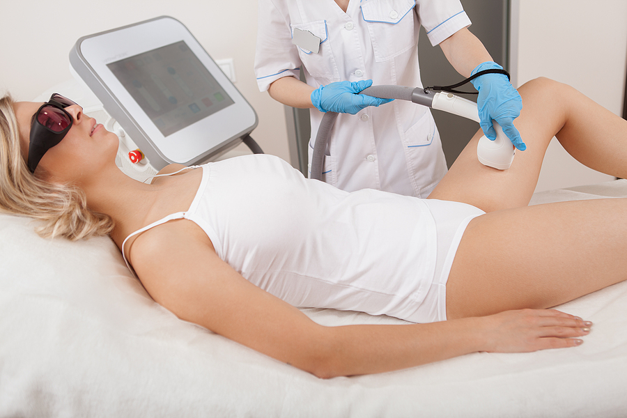 Attractive woman relaxing while cosmetologist removing hair on her thighs using laser hair removal machine
